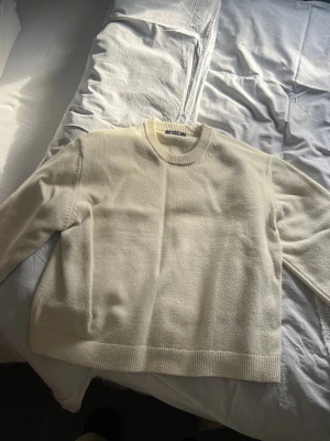 Krämvit stickad tröja  - Säljer en krämvit stickad tröja med rund hals och ribbade muddar. Tröjan har en avslappnad, oversized passform och är perfekt att styla med jeans eller kjol. Materialet ser mjukt och mysigt ut, och färgen är enkel att matcha.