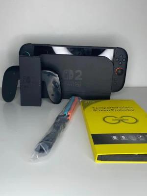Nintendo Switch 2 OLED med tillbehör - Nintendo Switch 2 OLED i svart med avtagbara Joy-Con-kontroller, dockningsstation och extra tillbehör som skärmskydd och färgglada handledsremmar. Konsolen har en stor skärm och klassisk design med rundade hörn och knappar i svart och orange. Knappt använd, kan köpa spel separat som finns i min profil, finns redan skärmskydd på och det finns en extra, det är fast pris .