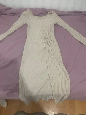 Beige ribbad långärmad klänning - Trendig beige klänning med ribbad struktur och lång ärm. Klänningen har en snygg twistdetalj i midjan som ger en unik look. Passar perfekt för dig som gillar stilrena plagg med det lilla extra.