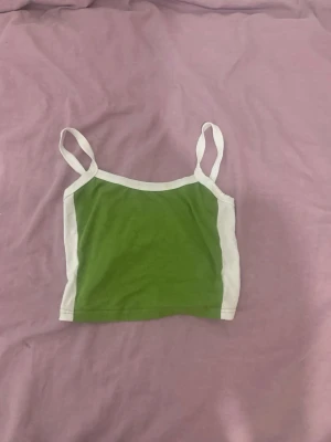 Grön och vit croppad linnetopp - Snygg croppad linnetopp i grön med vita kanter och smala axelband. Perfekt för varma dagar och enkel att matcha med jeans eller kjol. Tidlös och trendig design som ger en fräsch look.