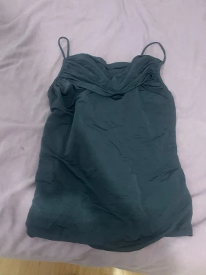 Mörkgrön linnetopp med tunna band - Snygg mörkgrön linnetopp med tunna axelband och draperad urringning. Perfekt för dig som gillar en enkel men stilren look. Passar till både jeans och kjol för en trendig outfit.