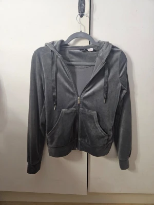 Grå velourhoodie från Gina Tricot - Jättefin och jättemjuk mörkgrå hoodie från Gina Tricot i velourmaterial. Tröjan har huva med snörning, dragkedja framtill och två stora fickor. Långärmad och med breda muddar vid ärmslut och nederkant. Nypris runt 200-300 kr. Säljer då jag inte får användning för den längre, men den är jättemjuk och skön att ha när det blir kallt. Mycket bra skick, endast använd väldigt få gånger. 💓