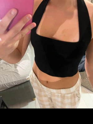 Svart halterneck topp från Zara - Snygg svart halterneck topp från Zara med breda axelband och croppad passform. Perfekt till höga byxor eller kjol. Materialet är mjukt och stretchigt, vilket gör den bekväm att bära. Enkel och stilren design som passar till många olika looks.