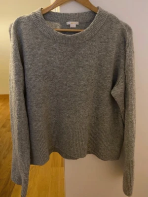 Grå stickad tröja från Gina Tricot - Mjuk och enkel grå stickad tröja från Gina Tricot med rund halsringning och ribbade muddar vid ärmslut och nederkant. Perfekt för lager-på-lager och passar till jeans eller kjol. 