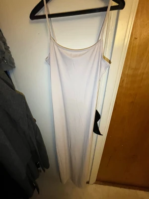 Ljus långklänning med smala axelband - En enkel och stilren långklänning i ljus färg med smala axelband och rak passform. Klänningen är ärmlös och har en mjuk, följsam känsla som passar perfekt till sommaren. Materialet känns lätt och bekvämt mot huden.