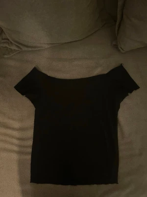 Svart offshoulder topp - En stilren svart offshoulder topp med korta ärmar. Toppen har en tight passform och är perfekt för dig som gillar minimalistisk stil. Tillverkad i mjukt stretchigt material som sitter snyggt på kroppen.