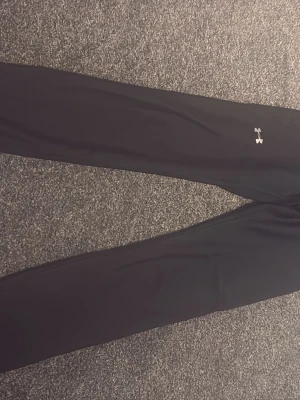 Svarta leggings från Under Armour - Säljer ett par svarta leggings från Under Armour med diskret logga på benet. De är tighta och stretchiga, perfekta för träning eller chill. Materialet känns mjukt och följsamt mot huden. Klassisk modell utan fickor eller detaljer.