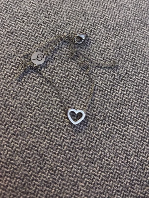 Silverhalsband med hjärthänge från Edblad  - Snyggt och stilrent halsband i silverfärgad metall från Edblad. Halsbandet har ett öppet hjärthänge och en tunn kedja med rund bricka vid låset där Edblads logga syns. Perfekt för dig som gillar minimalistisk design och vill ha något enkelt men ändå fint. Observera att det är en liten knut på kedjan vid låset, syns på bild tre men det gör ingen skillnad och syns inte. Aldrig använt och knuten har blivit av att de har åkt med i min necessär.