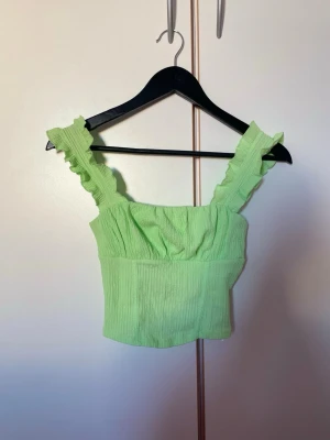 Ljusgrön volang topp med breda axelband - Supersöt topp i mintgrön med breda volangprydda axelband. Toppen är croppad och har en mjuk, stretchig känsla som passar perfekt till sommaren. 