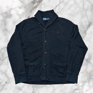 Ralph Lauren button up kofta - herr strl M - Säljer en Ralph Lauren svart button up kofta i storlek M med vinröd Ralph Lauren logga broderad på bröstet.  👕 Märke: Ralph Lauren 📏 Storlek: M 🎨 Färg: Svart 🧵 Material: 100% bomull 📐 Mått: 65 cm lång, 53 cm bred 📌 Skick: Mycket bra skick (se bilder)  💬 Hör av dig vid frågor 💰 Pris kan diskuteras vid snabb affär 📦 Skickas inom 24 timmar