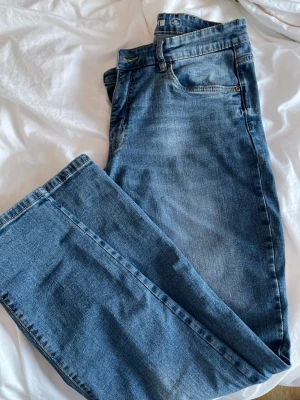 Blå raka jeans med hög midja - Säljer ett par klassiska blå jeans med rak passform och hög midja. Materialet är denim i bomull och färgen är mellanblå med lätt tvättad effekt.