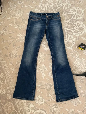 Blå bootcut Mavi  jeans med slitningar - Snygga blå bootcut Mavi  jeans med lätt slitna detaljer framtill och klassiska fem fickor. Jeansen har en låg midja och stängs med knapp och dragkedja. Perfekta för en avslappnad och trendig look.det står inget storlek på byxa ,men jag tror att det är storlek är nästan 38 .måttet på midjan är ca:38