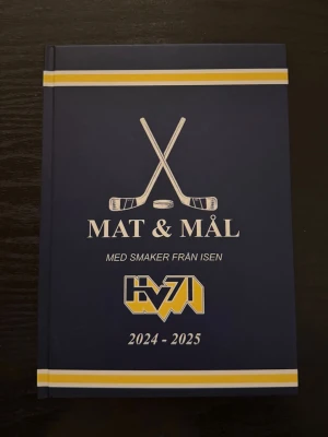 Mat & Mål HV71 2024-2025 - En mörkblå hårdbunden bok med hockeytema, fylld med recept och tips från HV71-spelare. Både herr och dam laget. Boken är från förra säsongen därav kan vissa spelare variera. Perfekt för dig som gillar både matlagning och hockey. Finns endast 12 exemplar då denna bok var mitt gamla UF företag. Vissa dam bilder är lite pixliga men ändrar verkligen inte kvaliten på boken💓skriv vid frågor 