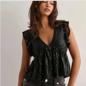 Svart glittrig volangtopp - Supersnygg svart blus med glittriga paljetter och volangdetaljer vid axlarna. V-ringning och luftig. Från Nelly, helt slutsåld. Använd en gång. 