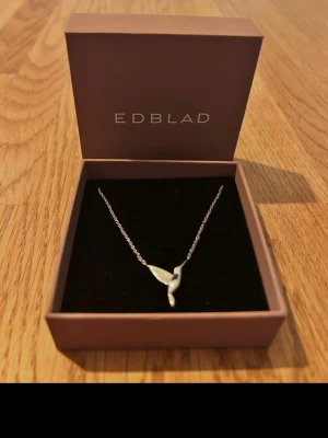 Silverfärgat halsband från Edblad - Har aldrig använt, nyskick. Snyggt halsband från Edblad i silverfärg med ett elegant hängsmycke som liknar en fågelvinge. Kedjan är tunn och smidig, perfekt för att lyfta vilken outfit som helst. Kommer i original ask med Edblad-logga.