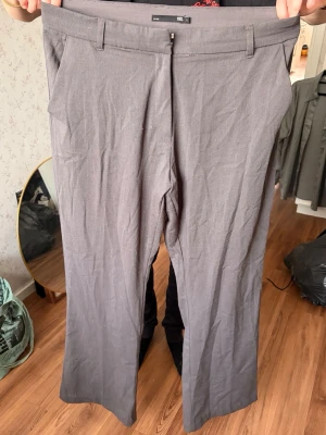 Grå kostymbyxor med raka ben - Snygga grå kostymbyxor med raka ben och klassisk passform. Byxorna har bälteshällor, snedställda fickor fram och två passpoalfickor bak. Perfekta för en clean och stilren look. Materialet känns mjukt och lätt. Hög midja. Obs hund finns i hemmet 