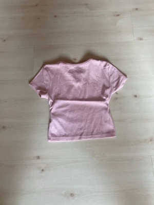  Ljusrosa t-shirt  - Söt ljusrosa t-shirt med korta ärmar och en liten v-ringad detalj vid halsen. 