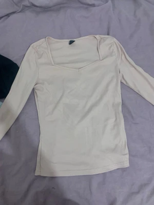 Ljusbeige ribbad topp med v-ringning - Säljer en ljusbeige ribbad topp med lång ärm och snygg v-ringad hals. Toppen har en figurnära passform och är perfekt att styla med jeans eller kjol. Enkel men trendig design som passar till många olika looks.