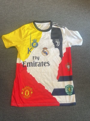 Ronaldo fotbollströja - Unik fotbollströja med Ronaldo-tryck och nummer 7 på ryggen. Tröjan har klubbmärken från Real Madrid, Juventus, Manchester United, Sporting Lissabon och Portugals landslag. Färgerna är gul, vit, röd, svart och blå med flera loggor och CR7. Fler frågor eller funderingar hör av er i dm!