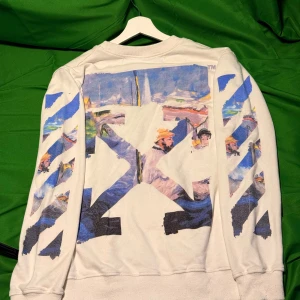 Vit Off-White tröja med konsttryck - Vit långärmad tröja från Off-White med ikoniska pilar och färgstarkt konstinspirerat tryck på ryggen och ärmarna. Crewneck-modell med svart Off-White-logga på bröstet. Snygg streetwear-vibe och unika detaljer i blått, lila och gult.Liknande modell som originalet!