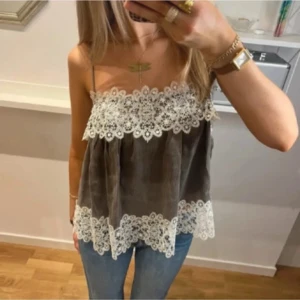 Grå manchesterlinne med spetsdetaljer - Supersöt grå linnetopp i manchester med tunna axelband och vita spetsdetaljer längs överkant och nederkant. Toppen har en luftig och flowy passform, perfekt för en trendig och avslappnad look.