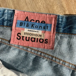 Acne Studios Blå Konst ljusblå jeans - Ljusblå jeans från Acne Studios Blå Konst med klassisk femficksdesign och orange kontrastsömmar. Jeansen har hög midja och raka ben, tillverkade i 100% bomull för en autentisk denimkänsla. Perfekta för en clean och stilren look.