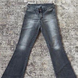 Grå bootcut jeans från Wrangler - Snygga grå jeans från Wrangler med bootcut passform. Jeansen har en cool tvättad look, ljusare partier och tydliga sömmar. Wrangler-logga på bakfickan ger extra stilpoäng. 39 cm i midjan tvärs över och 80cm innerben.