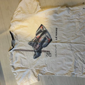 Vit GANT x Le Mans t-shirt med biltryck - Snygg vit t-shirt från GANT x Le Mans med coolt tryck av en racingbil på framsidan och stilrena linjer. Klassisk rund hals och korta ärmar. Perfekt för dig som gillar motorsport och vill ha en unik tee med sportig vibe.
