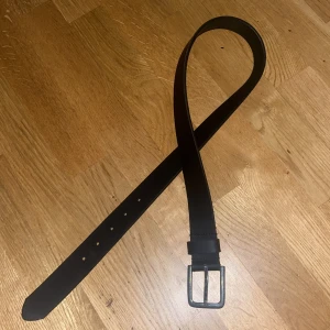 Svart skärp med silverfärgat spänne - Snyggt svart bälte med ett stilrent, fyrkantigt spänne i silverfärg. Bältet har en klassisk och enkel design som passar till jeans eller kostymbyxor. Materialet ser ut att vara skinn, vilket ger en tidlös och cool vibe. Perfekt för dig som vill ha en clean look.