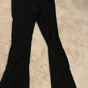 Svarta ribbade bootcut-byxor från SHEIN - Säljer ett par svarta ribbade byxor från SHEIN i storlek S. Byxorna har bootcut-ben och elastisk midja för skön passform. Materialet är mjukt och stretchigt, perfekt för dig som gillar en chill och trendig look.