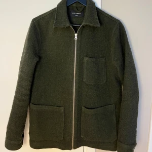 Mörkgrön jacka från A Day's March - Snygg mörkgrön jacka från A Day's March i ullmix. Jackan har tre stora utanpåfickor, rak passform och hel dragkedja framtill. Perfekt lager-på-lager-plagg med klassisk krage och stilren look.
