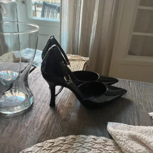 Svarta pumps med spetsig tå - Snygga svarta pumps med glansig finish och spetsig tå. Skorna har en smal klack och ett elegant ankelband med spänne 🥰
