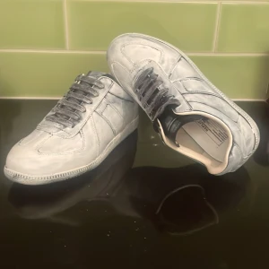Grå sneakers i skinn med snörning - Snygga grå sneakers med coolt marmorerat mönster. Skorna har rund tå, platt sula och klassisk snörning. Tillverkade i skinn med svart yttersula och vita detaljer på insidan. Perfekt för dig som gillar stilrena och unika sneakers.