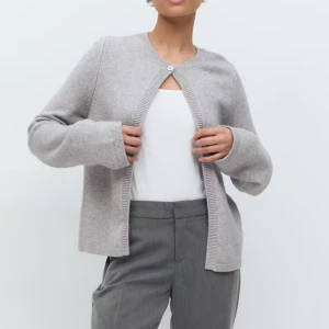 Grå kofta från Gina Tricot - Säljer en stilren grå kofta från Gina Tricot med rund halsringning och en knapp upptill. Koftan är i mjuk stickad kvalitet och har långa ärmar samt ribbade kanter. Perfekt att slänga över en topp för en clean look.