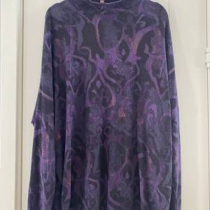 Mörklila polotröja med mönster - Säljer en oversized polotröja i mörklila med coolt abstrakt mönster i lila och svarta toner. Tröjan har ribbad hög krage och långa ärmar, perfekt för dig som gillar att sticka ut med din stil. Materialet är stickat och känns mjukt mot huden. Mått Över bröstet: ca 84 cm Längd från axeln och ner: ca 77 cm  74% viskos, 21% polyester och 5% elastan  Kommer från ett djur och rökfritt hem. 