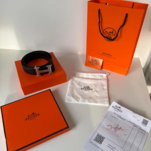 Svart H skärp med H-spänne - Exklusivt svart skärp från H med ikoniskt H-spänne i silverfärgad metall. Bältet är tillverkat i äkta skinn och har en stilren, klassisk design som lyfter vilken outfit som helst. Levereras med originalförpackning, dustbag och äkthetsbevis.