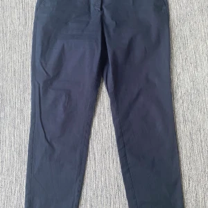 Marinblå chinos från Marc O'Polo - Snygga marinblå chinos från Marc O'Polo med klassisk rak passform och bälteshällor. Byxorna har framfickor och bakfickor med lock, tillverkade i mjuk bomull som känns skön mot huden. Perfekt för dig som gillar stilrena och enkla byxor. Mått Midjan: ca 51 cm Längd från grenen och ner: ca 75 cm  97% bomull och 3% elastan  Kommer från ett djur och rökfritt hem.