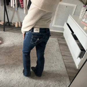 Mörkblå bootcut jeans från Miss Me - Snygga mörkblå jeans från Gina  med bootcut passform och kontrasterande vita sömmar. Bakfickorna har dekorativa knappar och broderade detaljer. Perfekt för dig som gillar en klassisk jeanslook med lite extra edge.