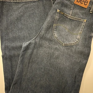 Lee Stella A Line wide jeans blå - Säljer ett par Lee Stella A Line jeans i klassisk blå tvätt med breda ben och hög midja. Jeansen har fem fickor, gul kontrastsöm och Lee-lapp bak. Materialet är slitstark bomullsdenim, perfekt för dig som gillar loose och trendig passform.