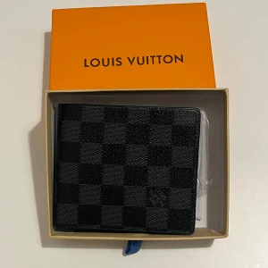 Svart rutig plånbok - Snygg svart plånbok med klassiskt rutigt mönster. Plånboken har flera fack för kort och ID, och är tillverkad i exklusivt skinn. Perfekt för dig som vill ha en stilren och lyxig accessoar i fickan.