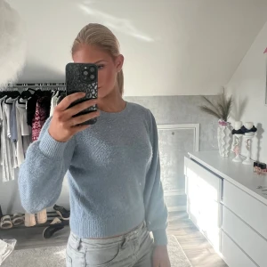 Ljusblå stickad tröja med rund hals - Säljer en ljusblå stickad tröja med rund hals och långa ärmar. Tröjan har en mjuk och skön känsla, ribbade muddar vid ärmslut och nederkant samt en klassisk passform som är enkel att matcha med jeans eller kjol.