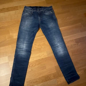 Replay Anbass jeans blå, stl 30 - Snygga blå Replay Anbass jeans i klassisk femficksmodell med lätt slitning. Jeansen har en modern tvätt, guldfärgade sömmar och är tillverkade i mjukt denimtyg som sitter skönt hela dagen. Hör av er för mer info