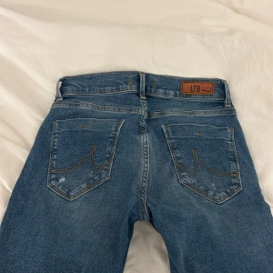 Blå jeans från LTB med slitningar - Säljer ett par klassiska blå jeans från LTB med snygga slitningar och ljus tvätt. Jeansen är bootcut, fem fickor och coola detaljer på bakfickorna. Perfekta för en avslappnad och trendig look.