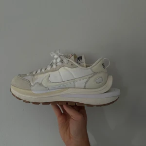 Nike X sacai VaporWaffle - White/Sail - Strl 43 - Limited Edition - Säljer ett par exklusiva sneakers från samarbetet mellan Nike och det japanska modehuset sacai.  Modellen är den ikoniska VaporWaffle med dubbla detaljer som dubbla sulor, dubbla swooshes och dubbla plösar – en av de mest eftertraktade silhuetterna från Nike de senaste åren.  Storlek: EU 43 (Sitter mellan 42 1/2 och 43 skulle jag säga) Skick: Begagnade men i bra skick. Mindre ytliga tecken på användning, sulan i gott skick (se bilder). Färg: White / Sail / Gum Ingår: Skorna utan originalkartong