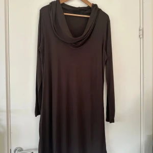 Brun långärmad klänning med polokrage - Mysig brun långklänning med lång ärm och en snygg polokrage som faller löst. Klänningen har en rak passform och är tillverkad i ett mjukt, stretchigt material som känns skönt mot huden. Perfekt för dig som gillar en enkel men stilren look. Lindex, strl L. 