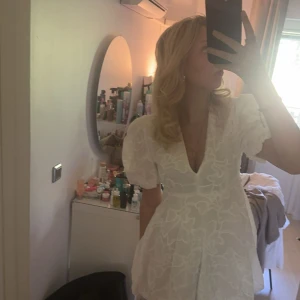 Vit zara klänning - Supersöt vit kort klänning med puffiga ärmar och djup v-ringning. Klänningen har ett broderat blommigt mönster och markerad midja som ger en fin siluett. Slutsåld Zara klänning som passar perfekt till student eller skolavslutning med ett otroligt blommönster på tyget. Lite för kort på mig som är 177 cm lång därav säljer jag den. Endast använd 1 gång