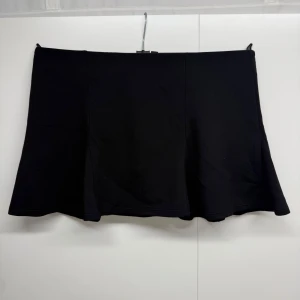 Svart minikjol  - Svart kortkjol från H&M Divided i storlek S. Kjolen har en enkel, utsvängd form och är tillverkad av en mjuk blandning av viskos, polyester och elastan. Inbyggda shorts på insidan gör den extra bekväm och praktisk. Perfekt för en chill och stilren look.