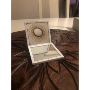 Vit sminkspegel från CAIA - Snygg och praktisk sminkspegel från CAIA i kompakt format. Spegeln har ett stilrent vitt plastfodral med CAIA-logga på framsidan och är perfekt att ha med i väskan för snabba touch-ups. Fyrkantig form och enkel att öppna och stänga. Spegeln är omsluten av plast, både på insidan och utanpå. 