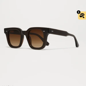 Chimi 04 - Snygga solglasögon med brun fyrkantig ram och tonade bruna glas. Modellen har en chunky retrostil med två silverprickar på varje sida av fronten. Passar dig som gillar statement-accessoarer och vill sticka ut med en cool look. 