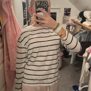 Randig långärmad tröja från 157 - Vit långärmad tröja från 157 med svarta horisontella ränder. Tröjan är i mjuk bomull och har en avslappnad passform med rund halsringning. Perfekt för en chill och enkel stil.